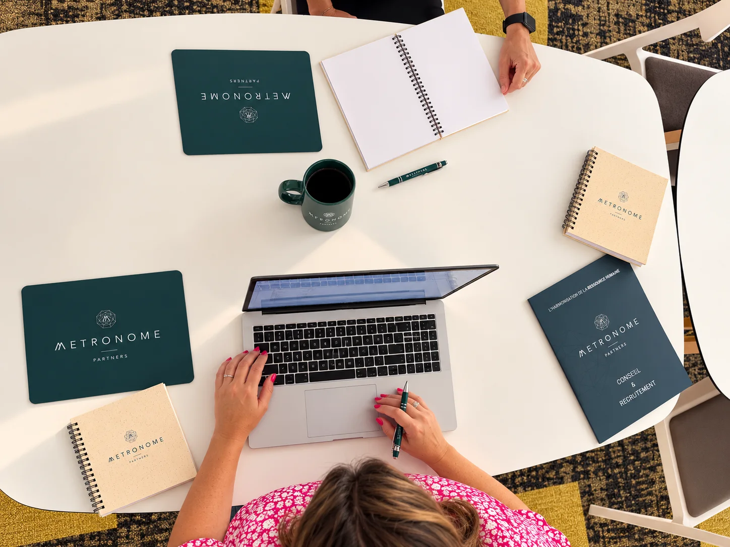 Contacter un cabinet RH : table de travail Metronome Partners vue du dessus, ordinateur, carnets et mug